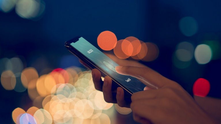 Someone performs fingerprint recognition on a smartphone, diffuse lights shine in the background