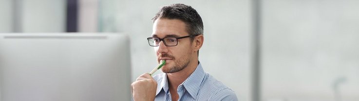 A man sits in front of a computer screen and holds a pen in his hand