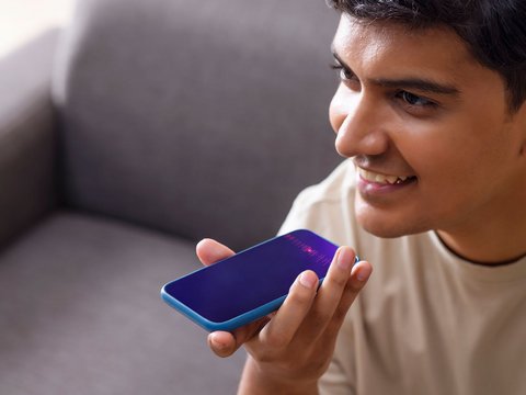 Smiling man using voice command on his smartphone while sitting on a couch.