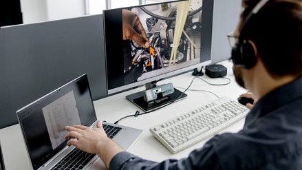 A professional working on a laptop and monitoring machinery repair on multiple screens.