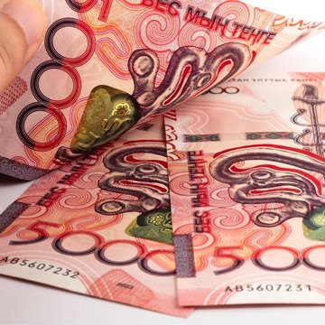 Three red new Kazakh 5000 Tenge banknotes with a man’s hand on them.