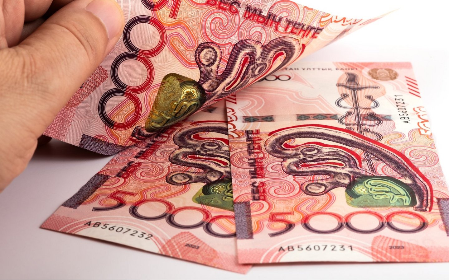 Three red new Kazakh 5000 Tenge banknotes with a man’s hand on them.