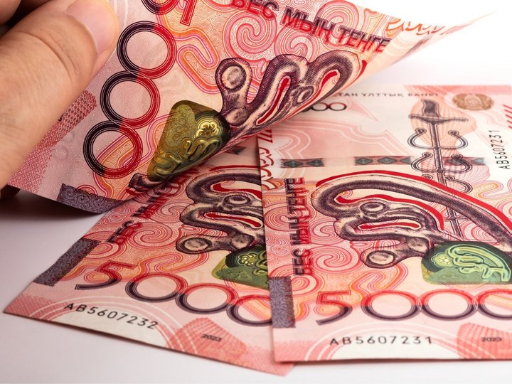 Three red new Kazakh 5000 Tenge banknotes with a man’s hand on them.