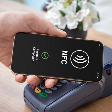 Male hand holds a smartphone to a pos terminal in order to pay via wireless technology (NFC)