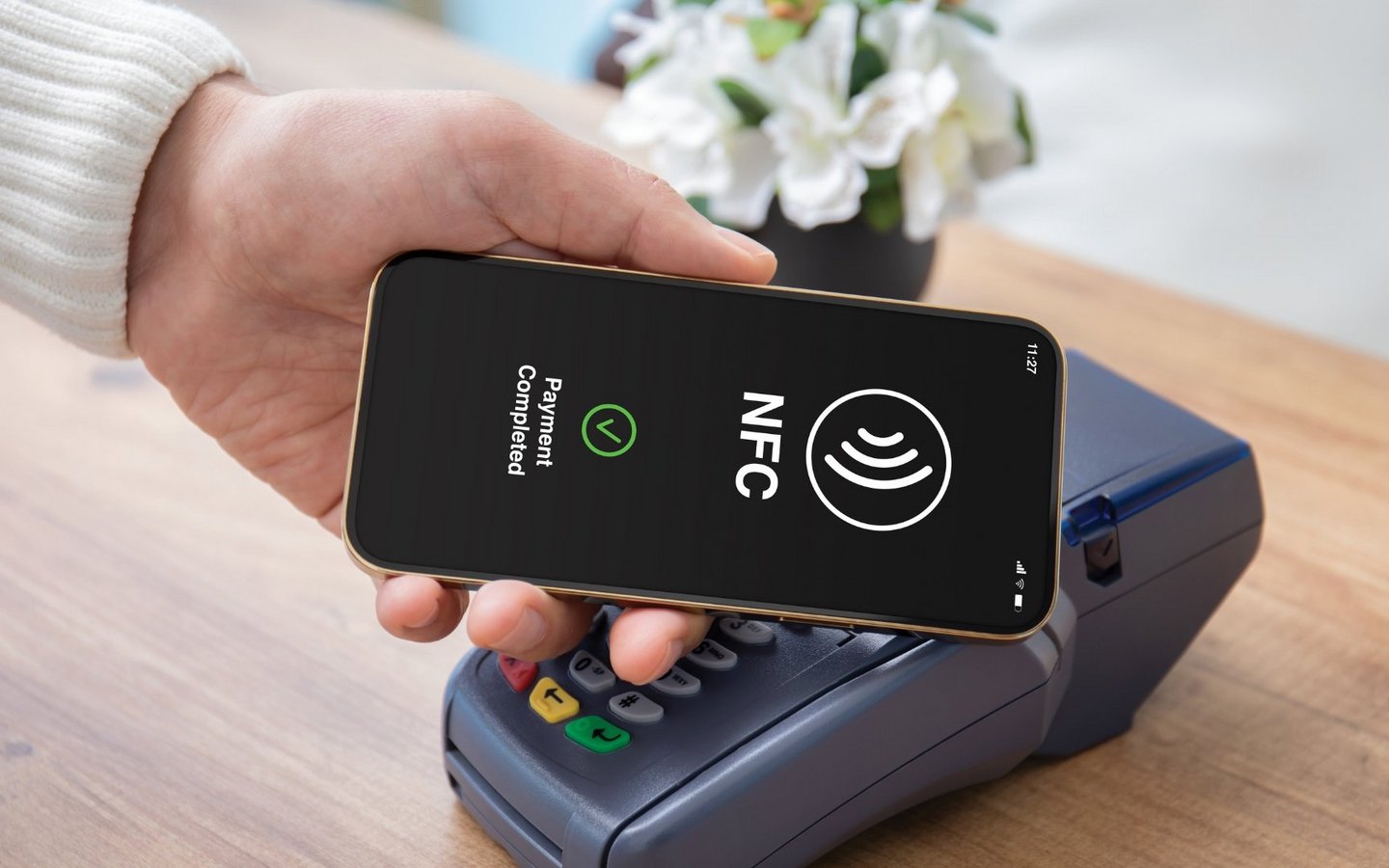 Male hand holds a smartphone to a pos terminal in order to pay via wireless technology (NFC)