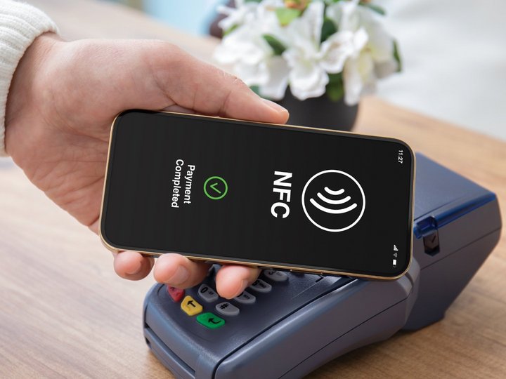 Male hand holds a smartphone to a pos terminal in order to pay via wireless technology (NFC)