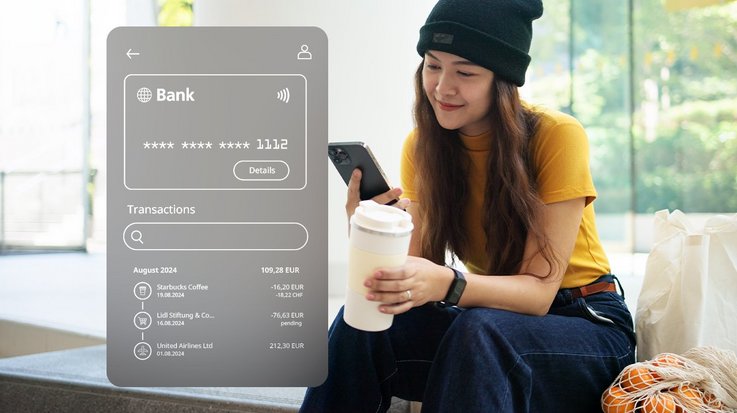 A person seated on a bench holding a coffee cup and a smartphone, viewing a digital banking interface displaying recent transactions.