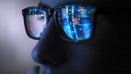 A luminous screen is reflected in the glasses of a man
