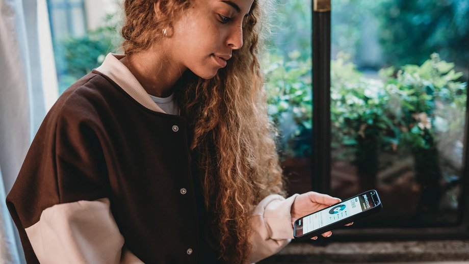 Young woman is checking her bank account. She’s holding a smartphone with a mobile banking app.