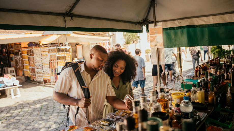 A young couple happily browses a market stall with spirits and local products
