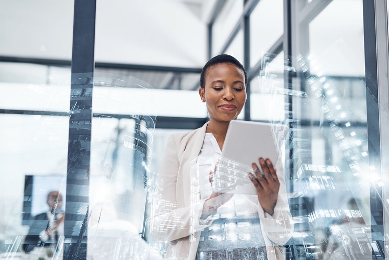 A businesswoman behind a window smilingly operates a tablet, there is a reflection of another office building