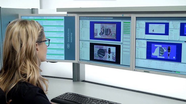 A woman sits at a desk with several computer screens
