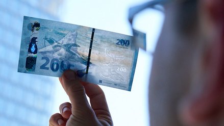 A man holds a banknote against the light, revealing various security features