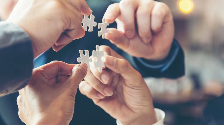 four people hold puzzle pieces together