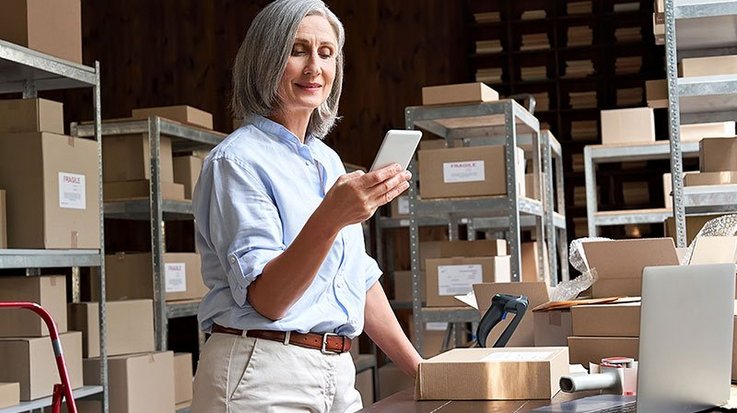 A woman stands in a storage room and uses her smartphone